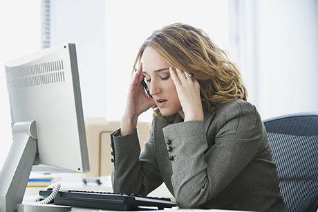 Stressed out woman sits at computer rubbing her temples 