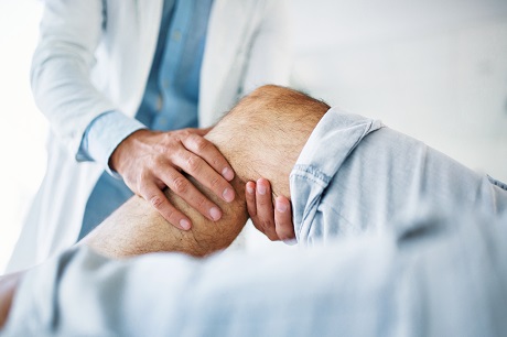 Therapist treating injured knee of athlete male patient.